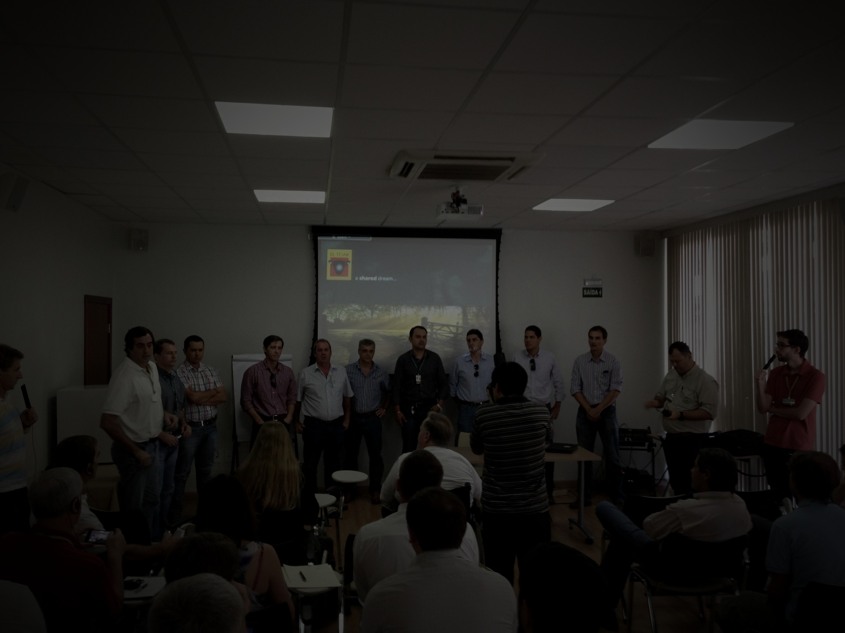 A distributor sales meeting in a dim room, the team in silhouette, a projector glowing on the wall