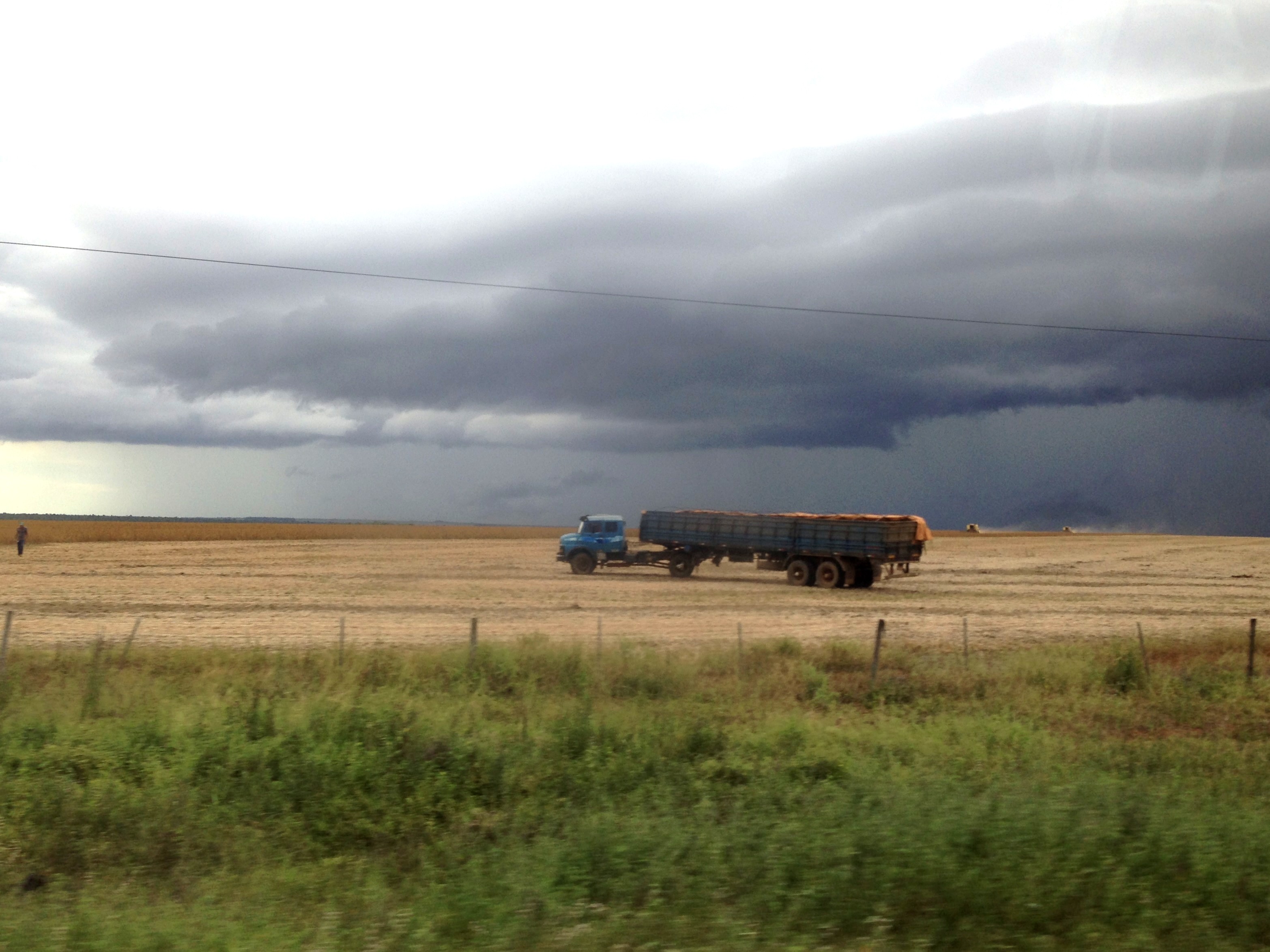 A loaded grain truck crossing a vast harvested field under a dramatic storm sky in Brazil